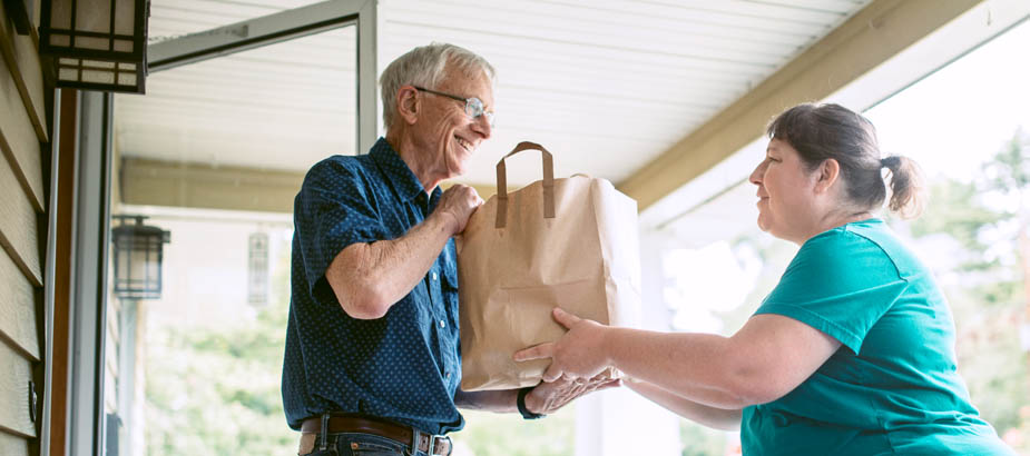 Woman Handing a Bag of Groceries to Man at Door