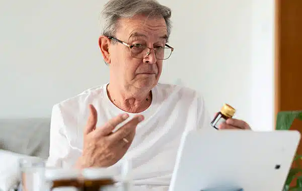 Man at computer looking frustrated while holding medicine bottle